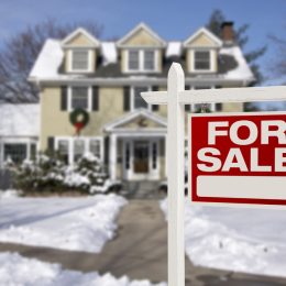 A "for sale" sign in front of a house covered in snow