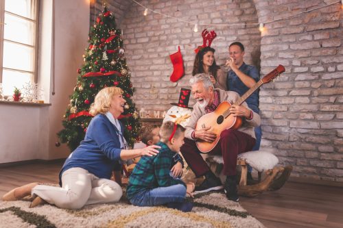 Beautiful happy family celebrating Christmas at home, gathered around Christmas tree, having fun while playing the guitar and singing Christmas songs