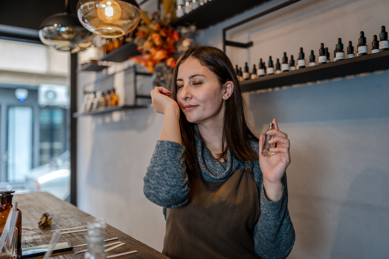 Young Perfumer preparing perfume while sitting at table in her own store