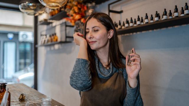 Young Perfumer preparing perfume while sitting at table in her own store
