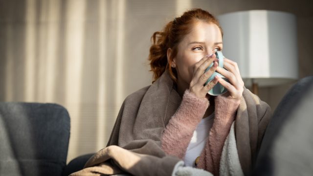 Woman wrapped in a blanket drinking from a mug.