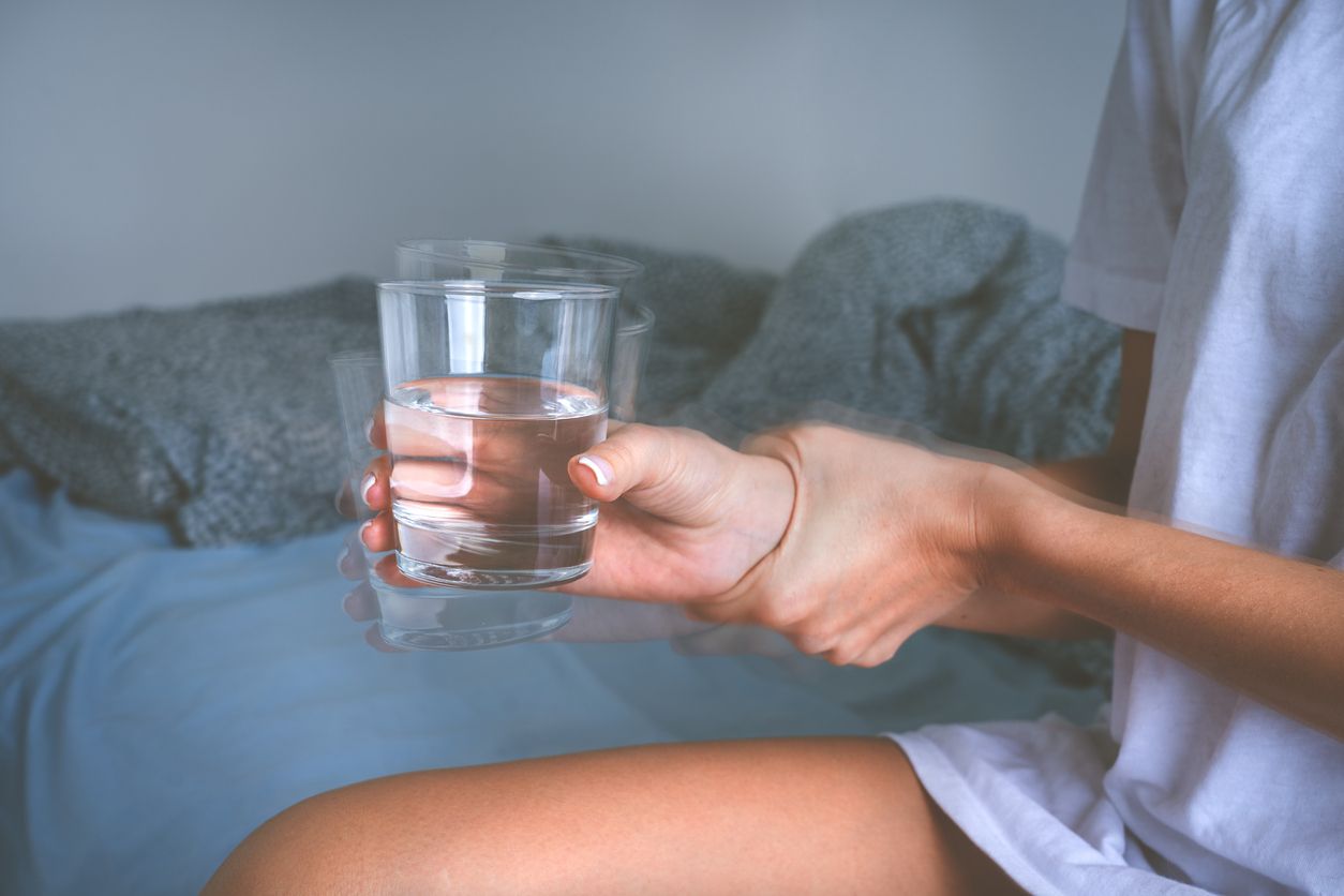 Person's hands with shaking and tremor, holding a glass of water.