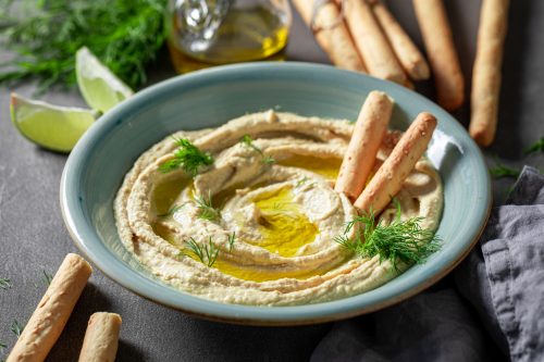 Tasty and homemade hummus with breadsticks, olive oil and dill. Hummus served with breadsticks and olive oil.