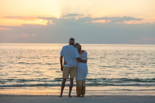 Mature man and woman hugging at sunset or sunrise on the beach.