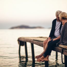 Senior couple sitting close together on a dock.