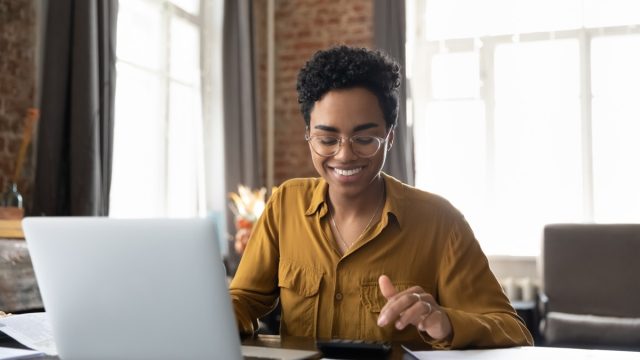 entrepreneur woman in glasses counting profit, on calculator at laptop computer, analyzing benefits, enjoying financial success, job high result, smiling