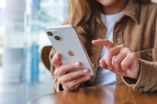 A close up of a woman sitting at a table and using an iPhone