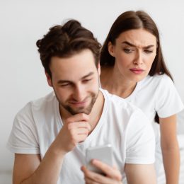 A suspicious-looking woman looking over her male partner's shoulder at his text messages.