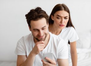 A suspicious-looking woman looking over her male partner's shoulder at his text messages.