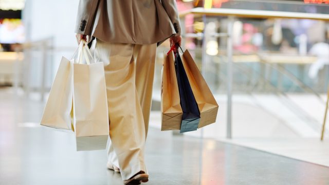 Low section of unrecognizable woman wearing pants and holding blank shopping bags while walking in mall, copy space