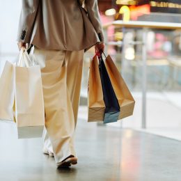 Low section of unrecognizable woman wearing pants and holding blank shopping bags while walking in mall, copy space