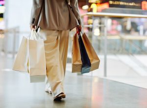 Low section of unrecognizable woman wearing pants and holding blank shopping bags while walking in mall, copy space