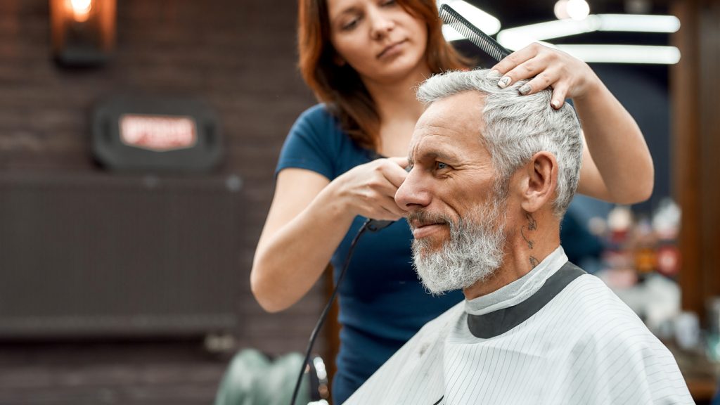 A senior man with gray hair sitting with a stylist and getting a haircut