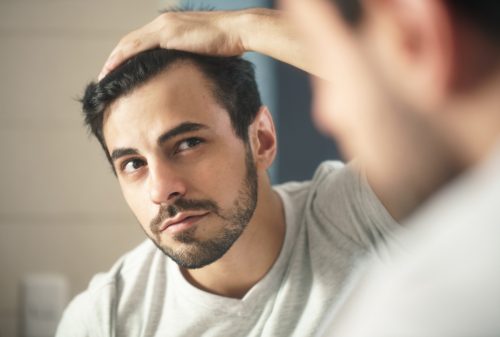 Man shaving in his bathroom at home. Caucasian metrosexual man worried about hair loss and looking in the mirror at his receding hairline.