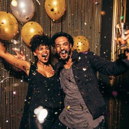 An energetic young couple celebrating the holidays with gold balloons and confetti around them.