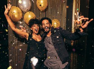 An energetic young couple celebrating the holidays with gold balloons and confetti around them.