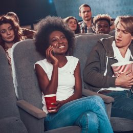 A young woman smiling and talking on the phone in the movie theater, while everyone around her looks annoyed.