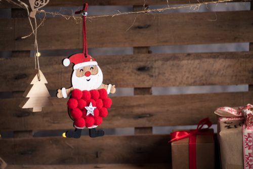 A wood Christmas tree and Santa ornament handing against a wood background.
