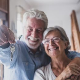 A senior couple hugging while holding keys to a new home