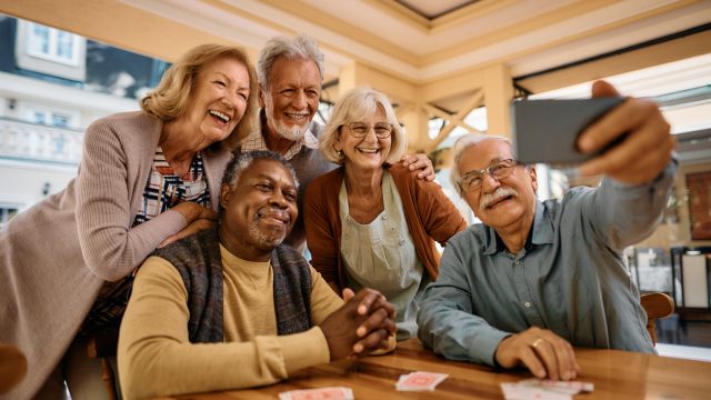 A group of five seniors taking a selfie in a retirement community lounge
