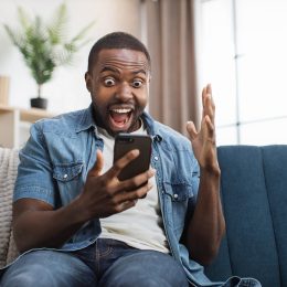Overjoyed man celebrating success with yes gesture while getting some goods news on mobile phone.