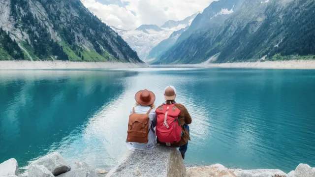 A couple in their 60's sitting by a lake surrounded by mountains.
