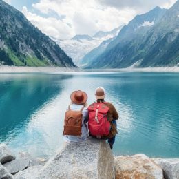 A couple in their 60's sitting by a lake surrounded by mountains.