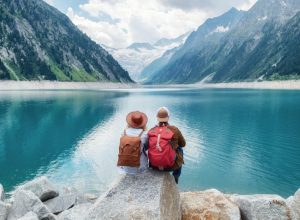 A couple in their 60's sitting by a lake surrounded by mountains.