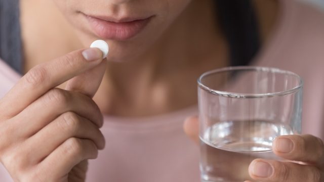 Woman taking a pill with water.