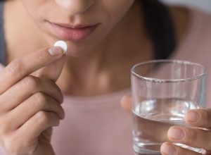 Woman taking a pill with water.