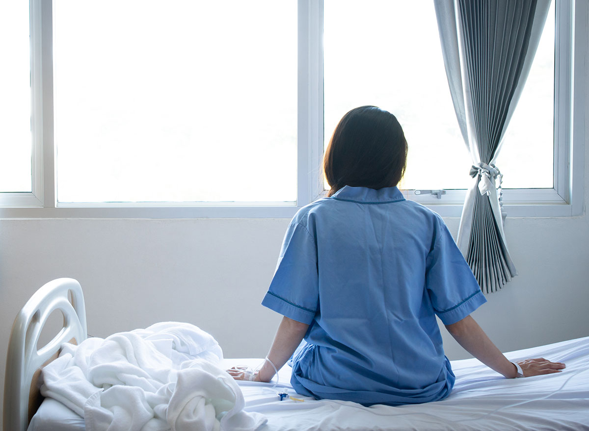woman sitting on edge of hospital bed looking out the window