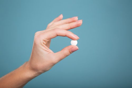 Woman holding up a pill with a blue backround. 