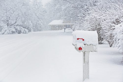 A row of three snowcapped rural residential roadside mailboxes during a blinding winter blizzard.