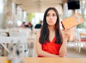 An ungrateful-looking young woman holding out a gift while sitting at a restaurant.