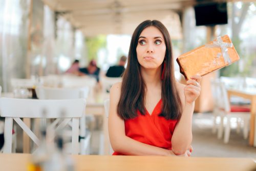 An ungrateful-looking young woman holding out a gift while sitting at a restaurant.