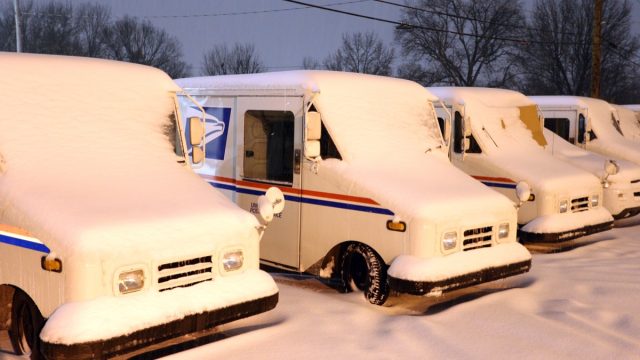Postal delivery trucks are being buried in snow during a snowstorm in Olivette, Missouri. Olivette is a suburb of St. Louis, Missouri.