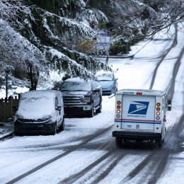 United States Postal Service (USPS) delivery truck driving down a snowy residential street during a winter storm, with space for text