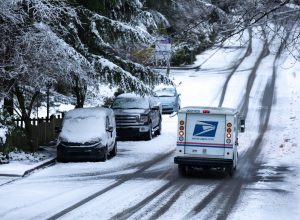 United States Postal Service (USPS) delivery truck driving down a snowy residential street during a winter storm, with space for text
