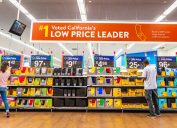 People shopping for back to school items in one of the Walmart stores; Banner advertising the low price leader status in California displayed above