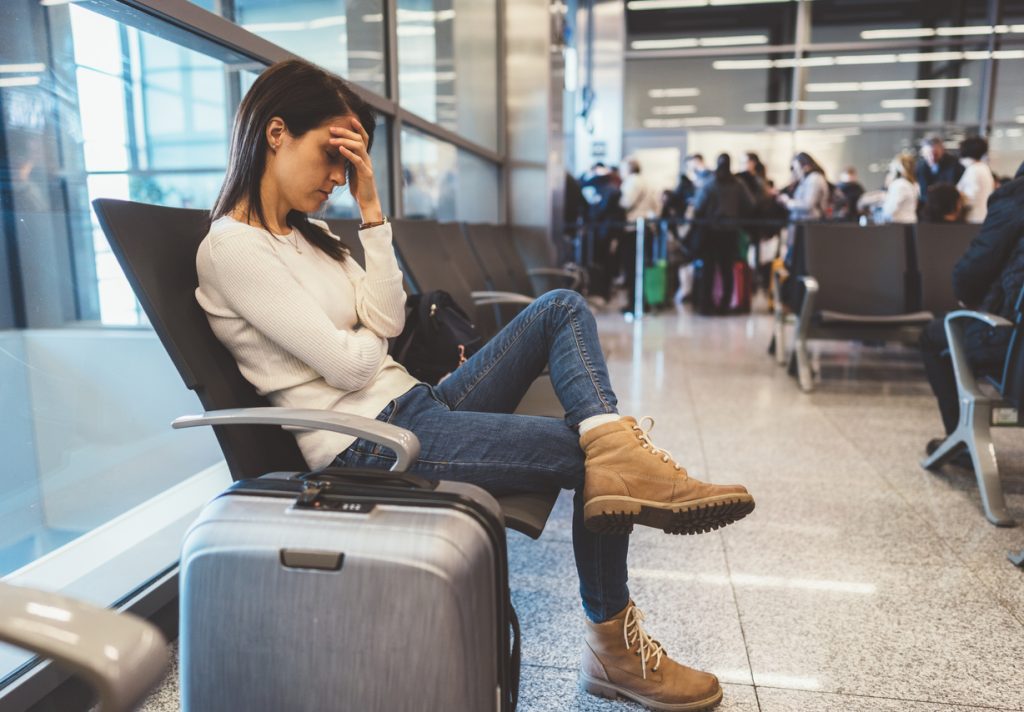 A young woman sitting at the airport with her head in her hands and a tired look on her face