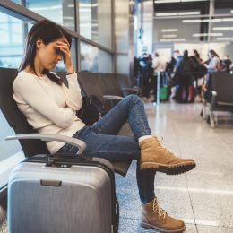 A young woman sitting at the airport with her head in her hands and a tired look on her face