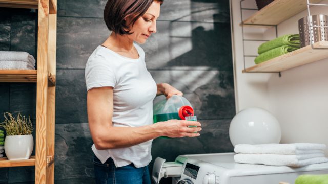 A woman measuring laundry detergent in the cap to pour into a washing machine