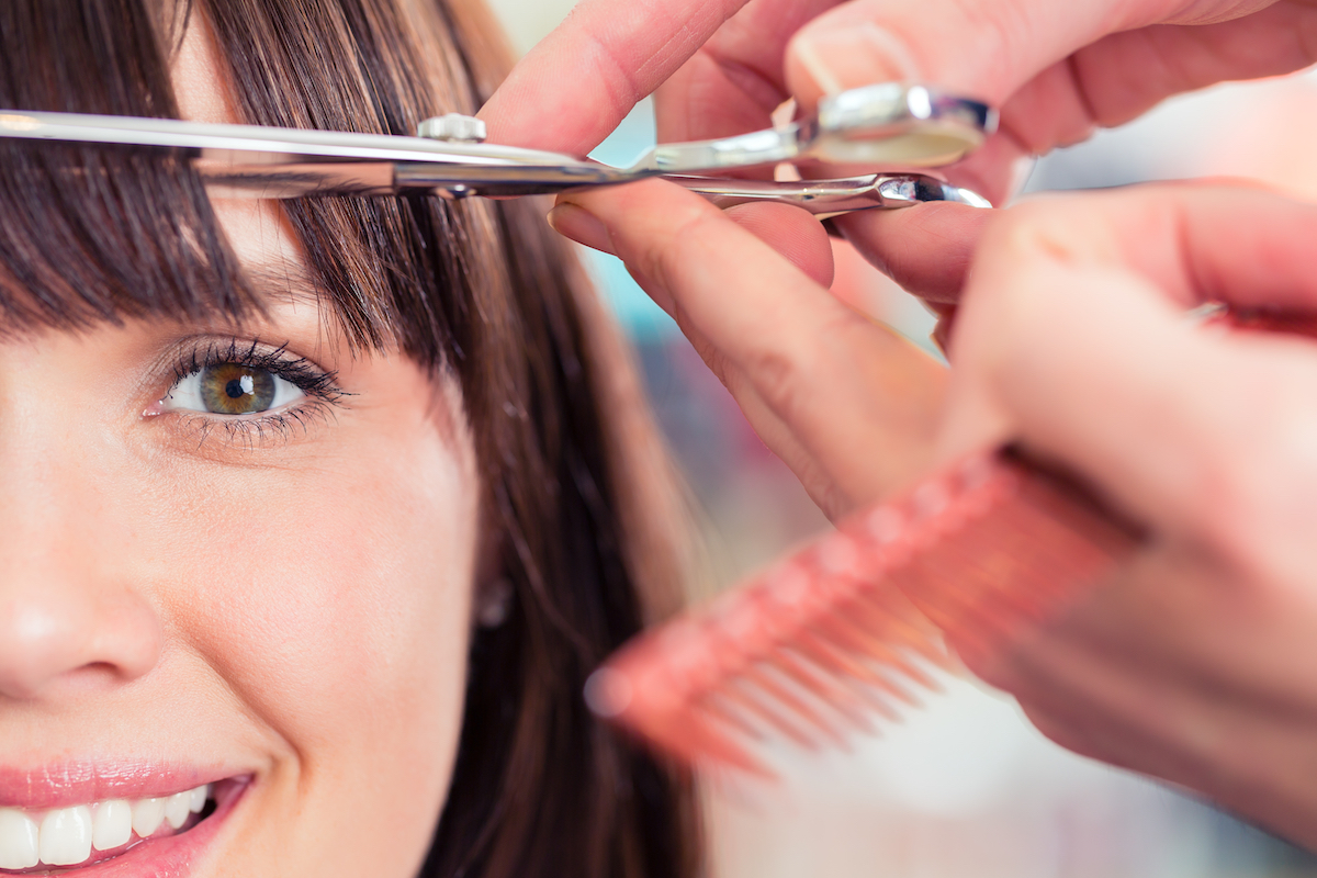 Close up of a brunette woman getting her bangs trimmed.