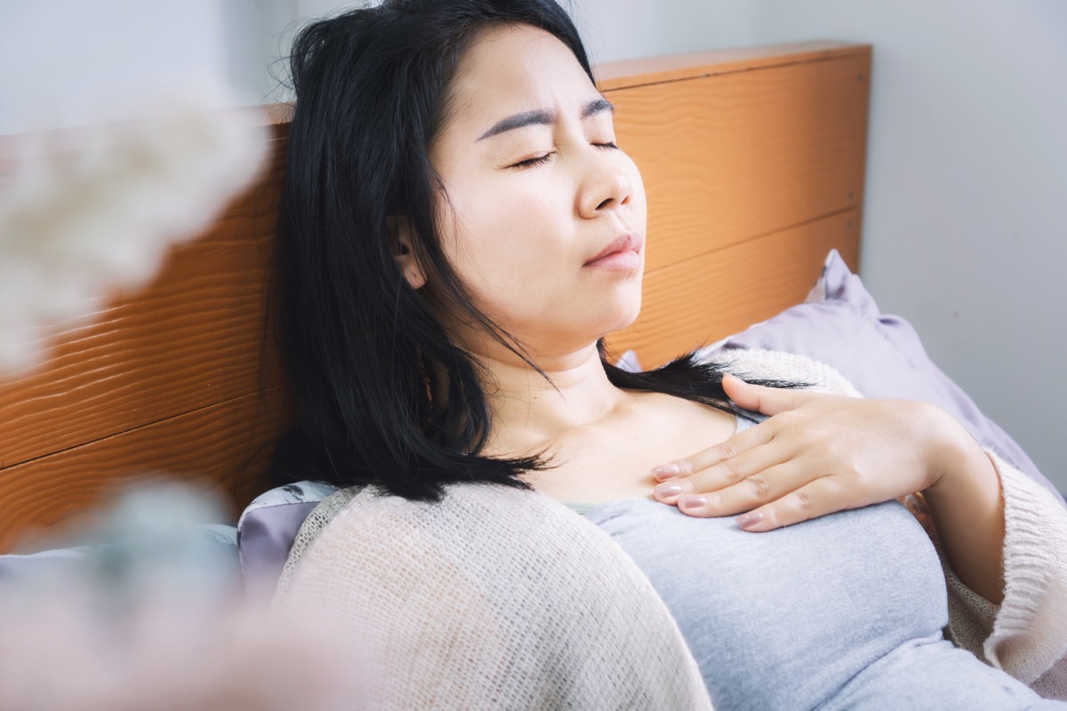 Asian woman laydown in bed having problem with heartburn from acid reflux difficult to breathe after wakeup in morning