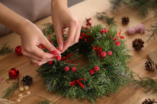 Close up of a florist making a beautiful Christmas wreath with berries at a wooden table 