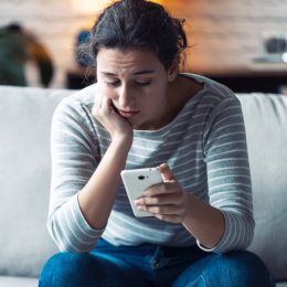 A young woman sitting on a couch and looking at her phone with a concerned expression on her face