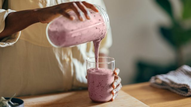 A close up of a woman pouring a smoothie out of a blender into a glass