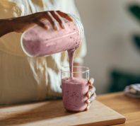 A close up of a woman pouring a smoothie out of a blender into a glass