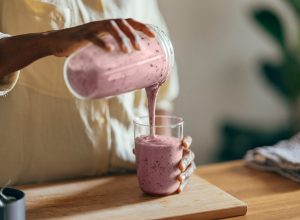A close up of a woman pouring a smoothie out of a blender into a glass