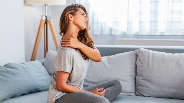 Woman sitting on her couch with neck pain.